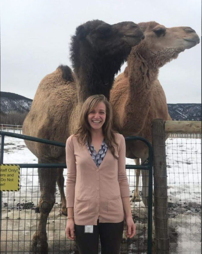 Community Engagement Manager, Nicole Borgione, stands in front of two camels